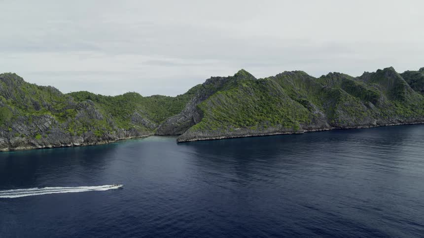 Boat sails out at sea passing by large mountains on an island