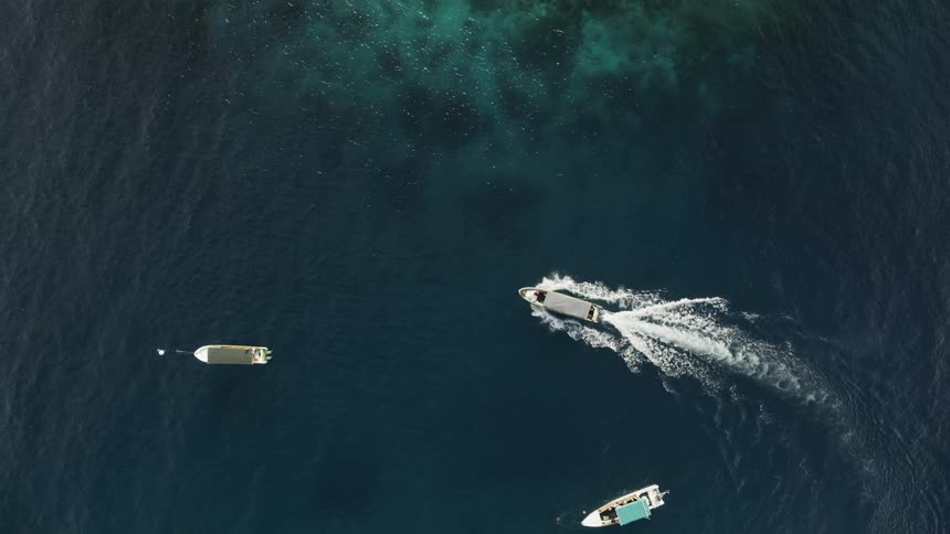 A boat moves past two boats anchored in a body of water