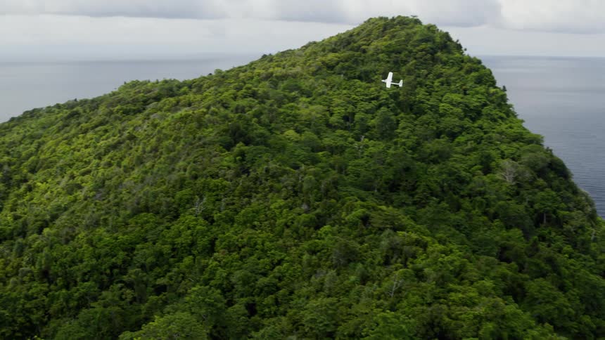 A small airplane flies over shoreline of ocean and over islands on an overcast day