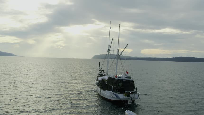 A boat with flags on the water near the coast with land the sky and clouds in the background