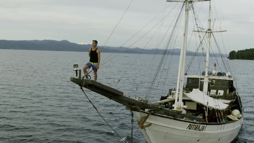 A man standing on a boat with the ocean land the sky and clouds in the background