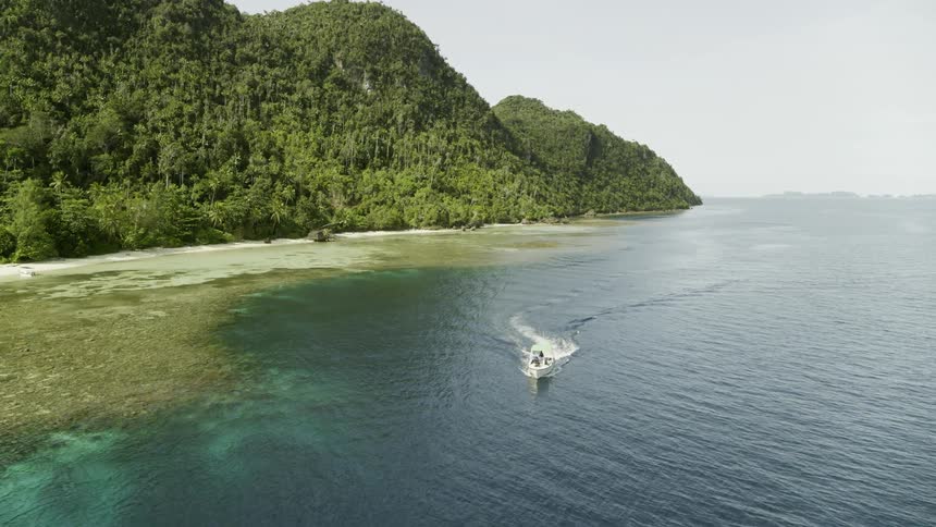 A boat drives on the water with an island and shoreline in site during the day