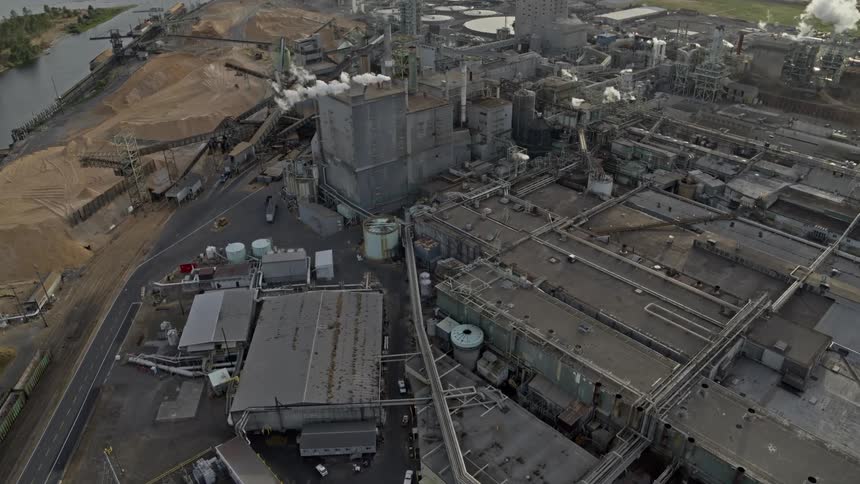 Smoke and steam rise from factory buildings along an industrial wasteland