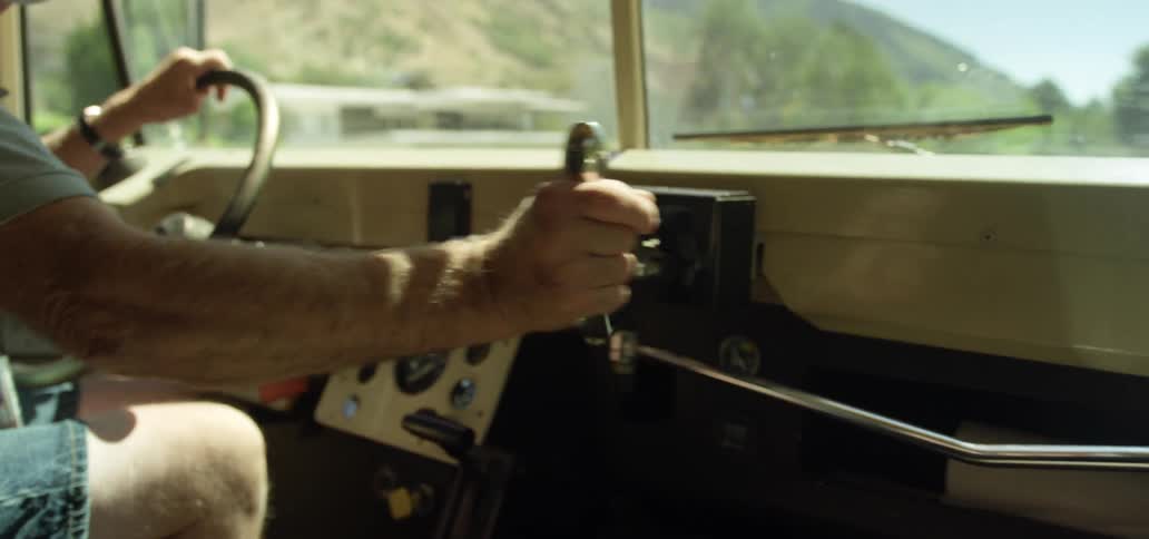 Man sitting in drivers seat on bus turning a door opening mechanism