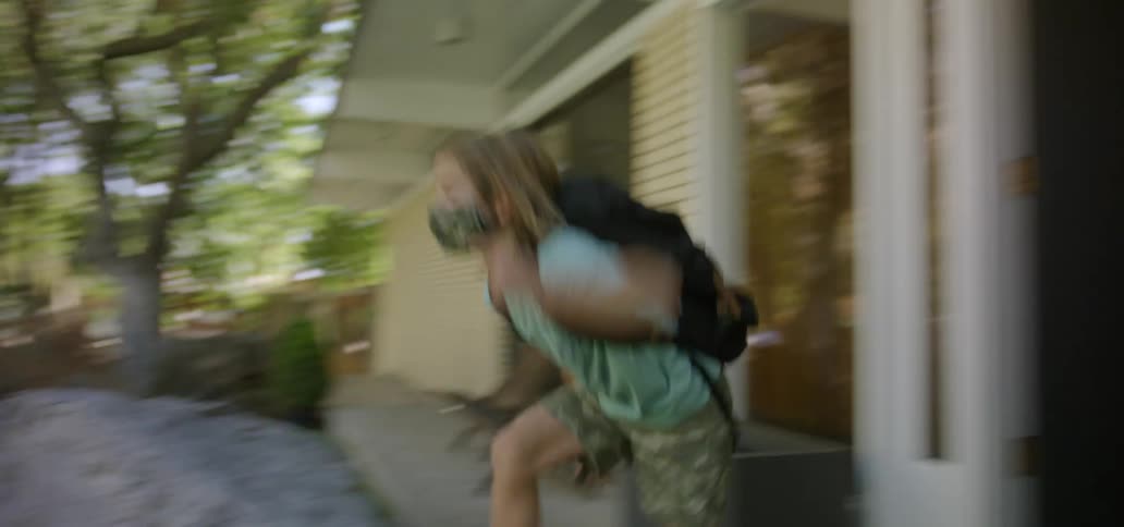 A young boy wearing a mask runs out of his house