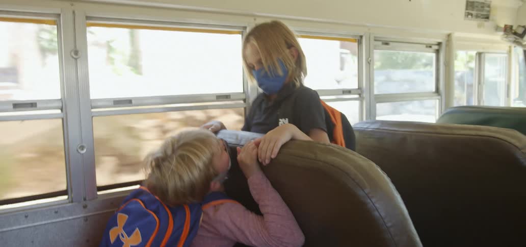 A boy is shaking another boys head on a school bus driving down a street