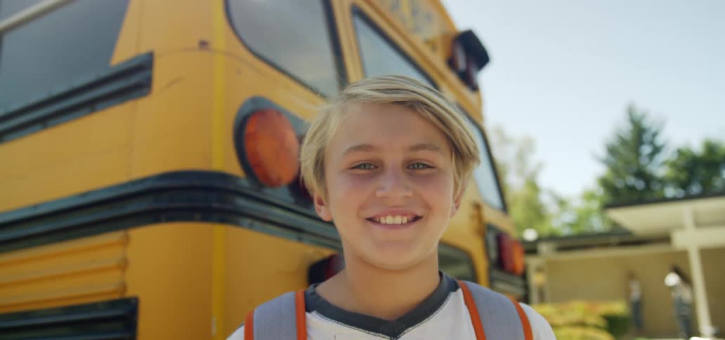 A young boy standing in front of a school bus parked at a school