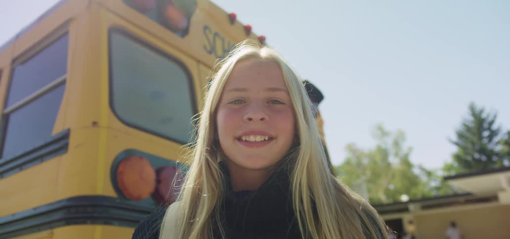 A girl is smiling by the school bus