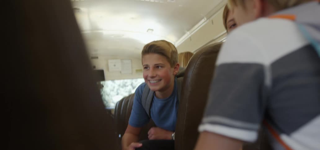 Boys and girls sitting on a moving school bus talking to each other