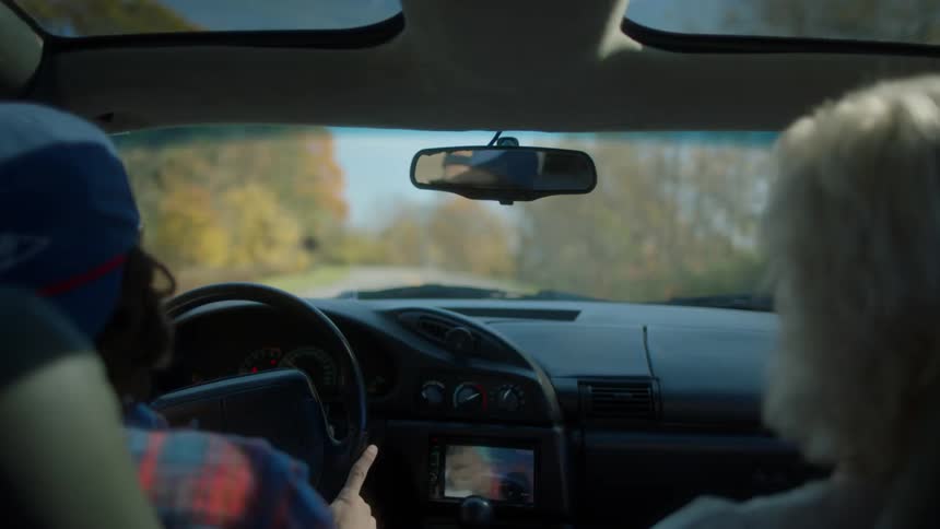 A man drives a car with an elderly woman in the passenger seat