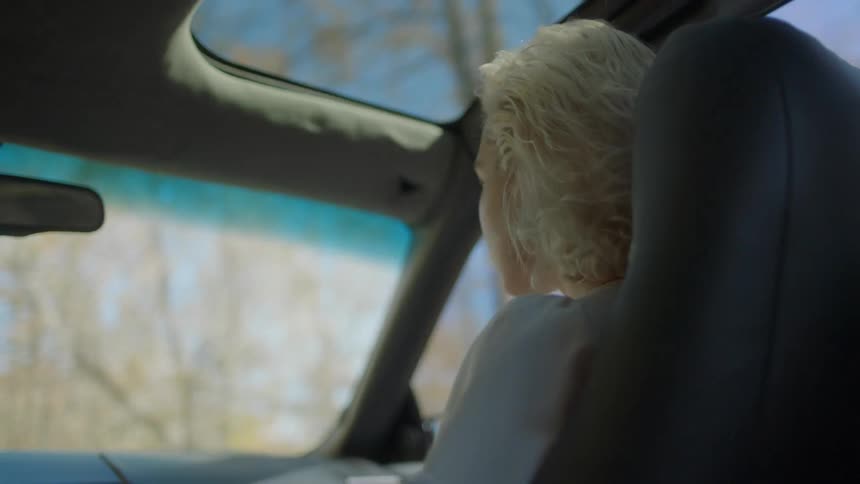Woman riding in a car past some trees