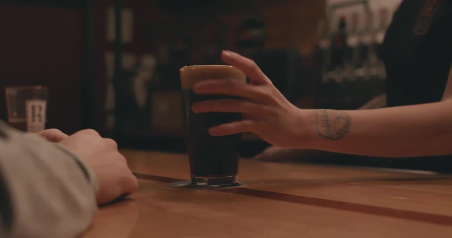 A woman bartender hands a patron a beer in a glass
