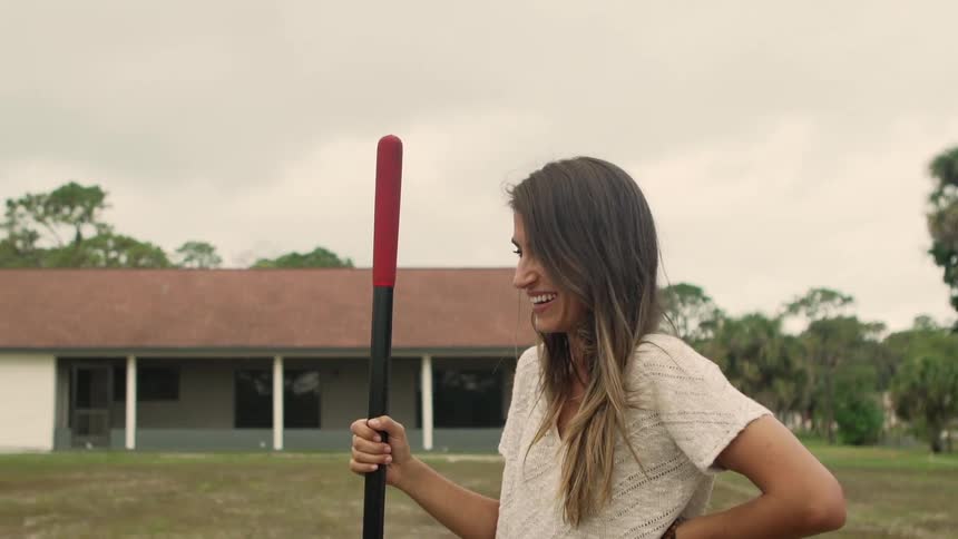 A woman holding a tool with a building trees the sky and clouds in the background