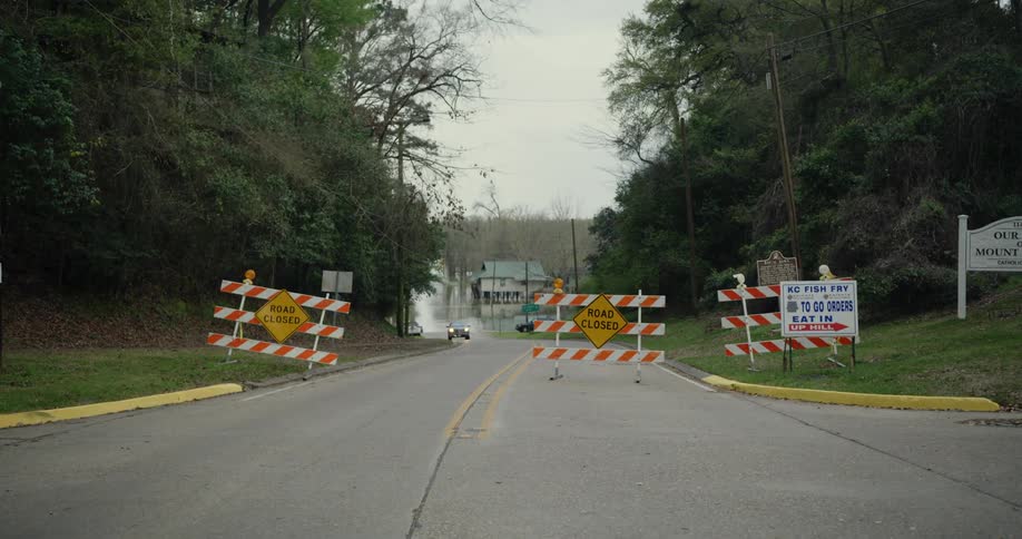 A pickup truck turns around to avoid flood waters at the bottom of a hill on a cloudy day