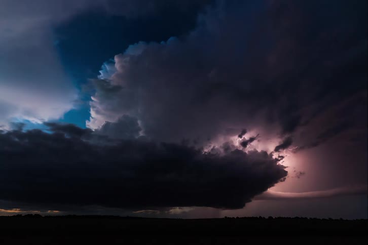 Lightning strikes between dense clouds over a city