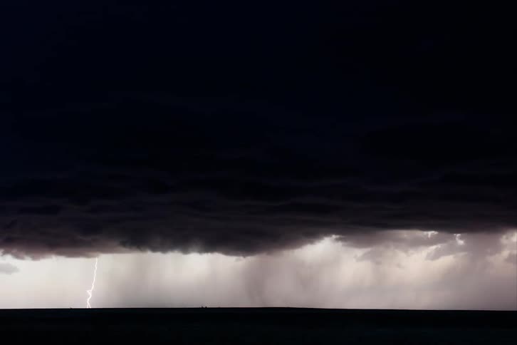 Bolts of lightning strike a grassland from dark clouds swirling in the sky above