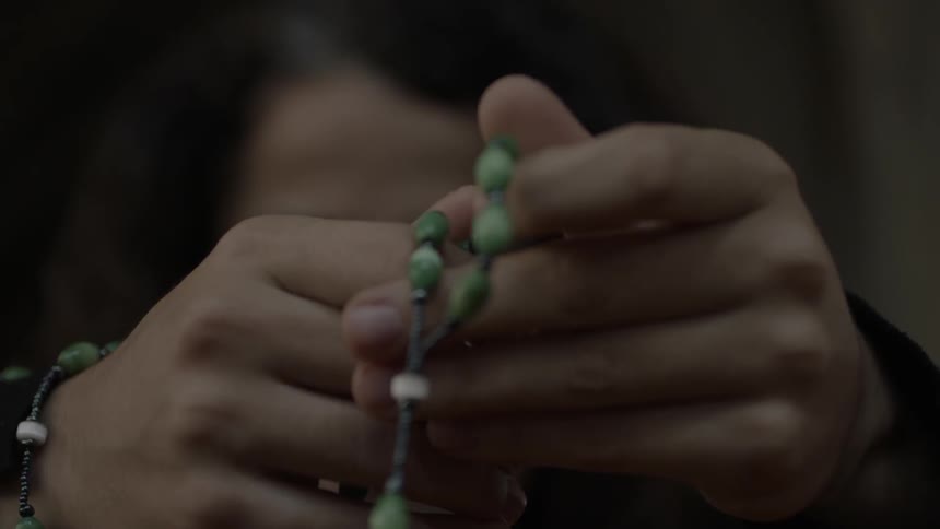 Two hands clasp a rosary