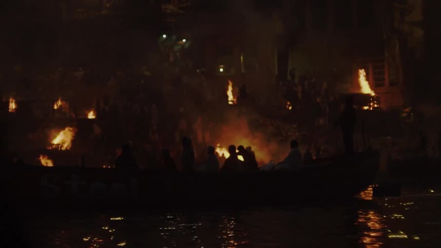 A boat full of people take in a display where homes on the side of a mountain are on fire