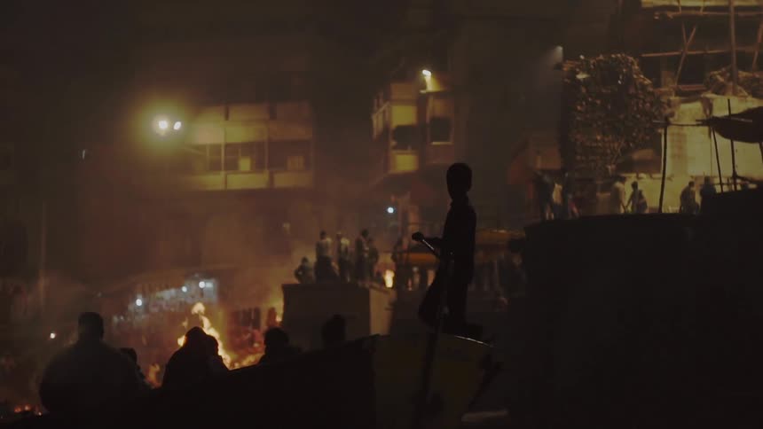Silhouettes of people on a boat with fires and buildings in the background