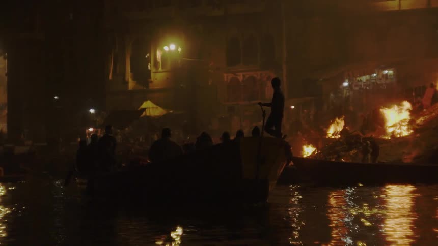 Silhouettes of people on boats with fires and buildings in the background