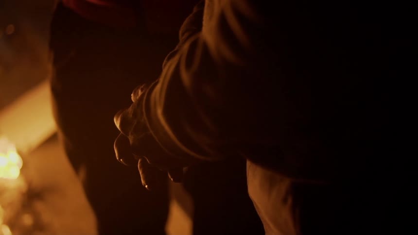 A person folding their hands with fire burning and smoke in the background