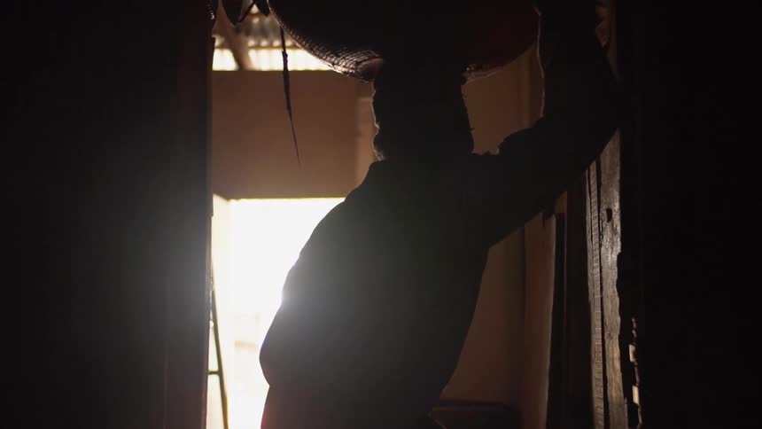 Person balances large bowl on their head moving down corridor past ladder toward outside