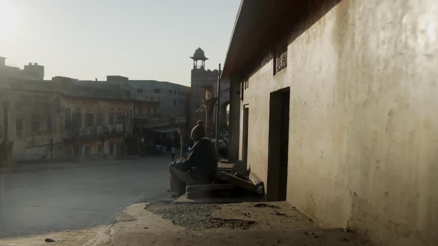 A horse moves its tail as it waits outside a building where a statue of a man is shown sitting while holding a stick