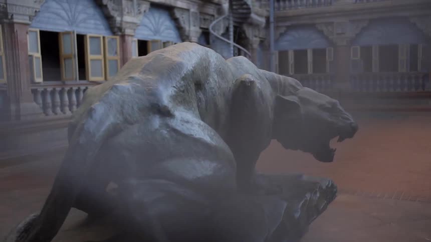 A sculpture of a panther with a fence in the foreground and a building in the background