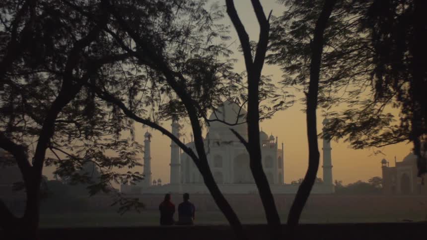 Two people sit on a bench in front of the taj mahal in hazy weather