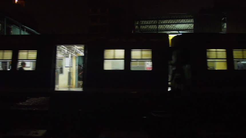 Silhouetted passenger train at night with people standing and waiting onboard