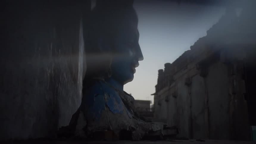 A sculpture of an asian mans head runs the height of an ancient building