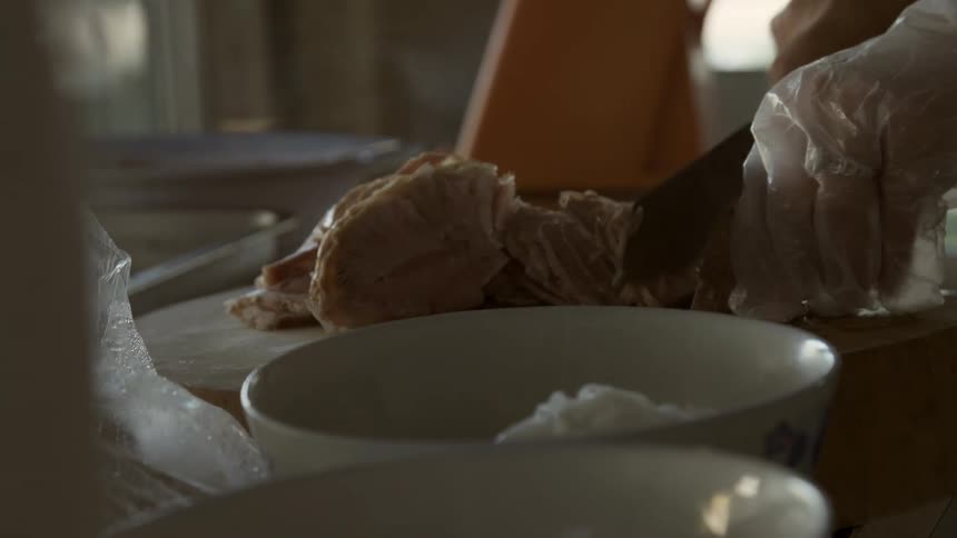 A person wearing gloves carefully cuts meat with a large knife