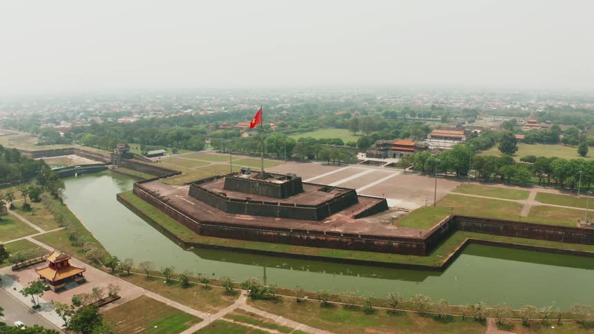 A wide moat surrounds a pentagon shaped building with a red flag flying on top