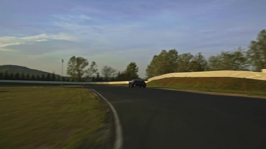 A black car is driving on a black race track outside in the sun