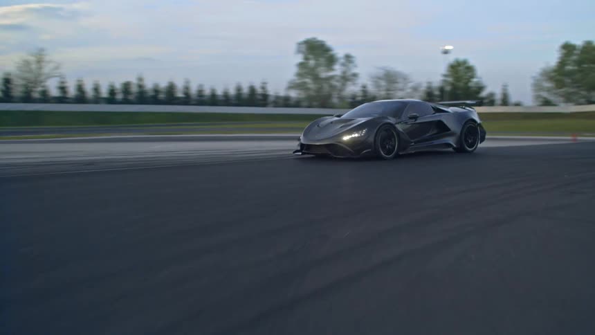 A car is driving on a racetrack at dusk