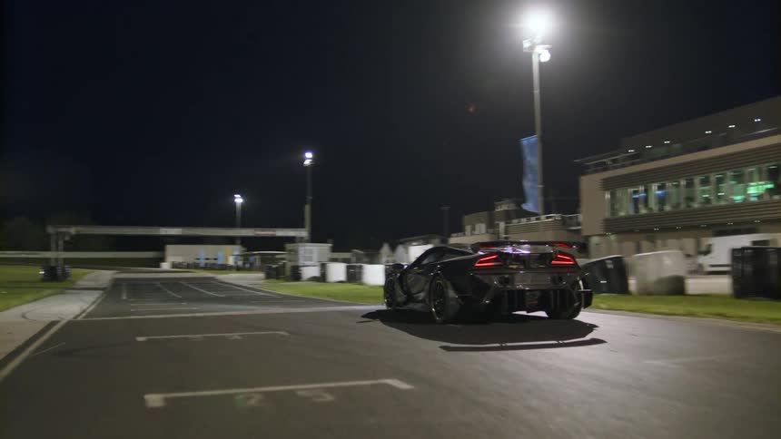 A car is driving on a racetrack at night