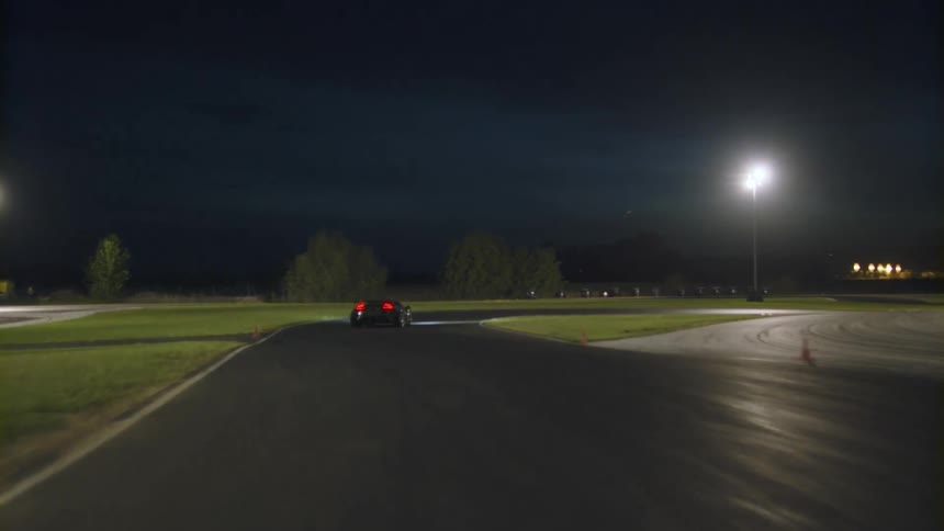 A black sports car slows around a curve on a track then picks up speed
