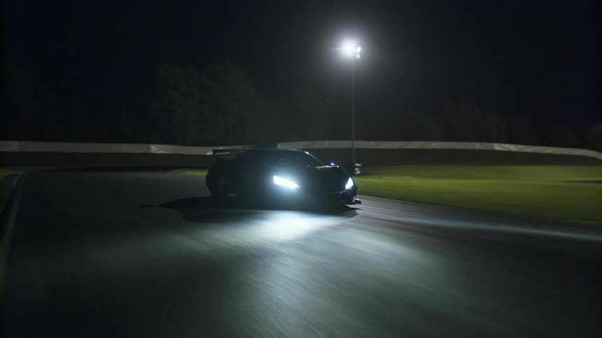 A black sports car drives on a curved track at night