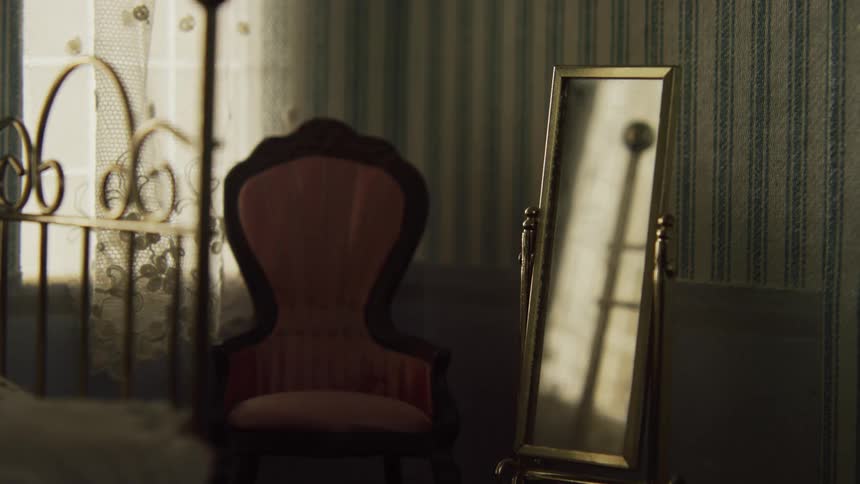 An antique chair and full length mirror sit at the foot of a gold framed bed