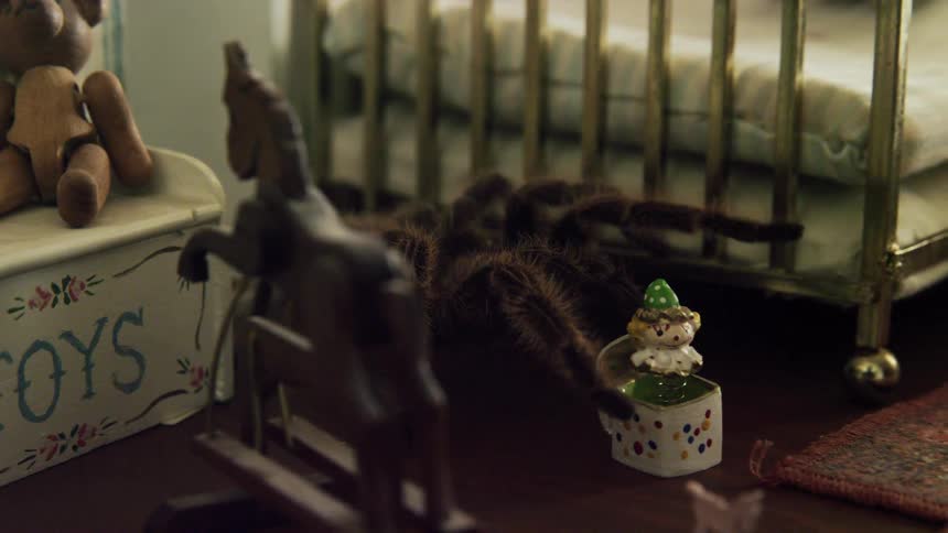 A hairy tarantula crawls on a toy rocking horse in a doll house