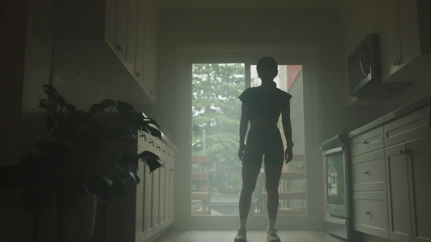 A woman in workout clothing stands in her narrow kitchen