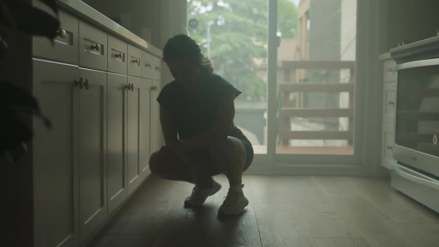 A woman crouches in a kitchen
