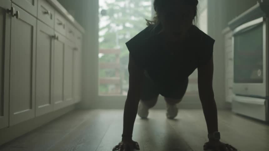 Woman doing push ups is silhouetted against the kitchen door in the kitchen