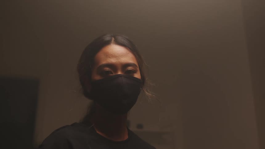 A woman is standing in a room and wearing a face mask