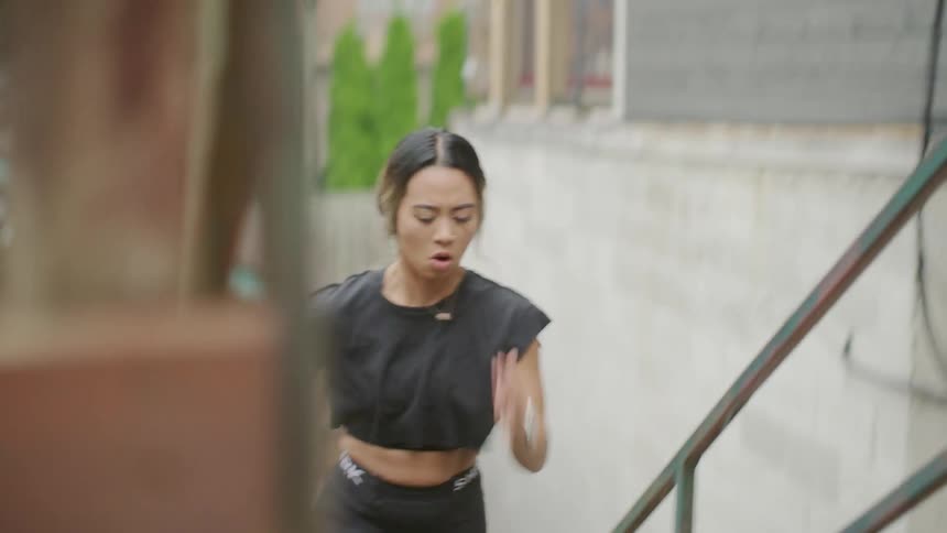 An asian woman runs up exterior stairs in a sprint during the day