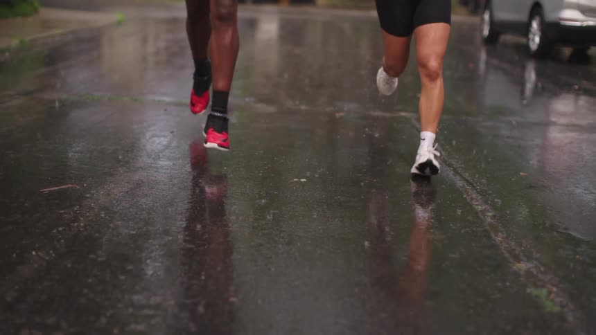 Man and woman in workout attire running down a neighborhood street in the rain