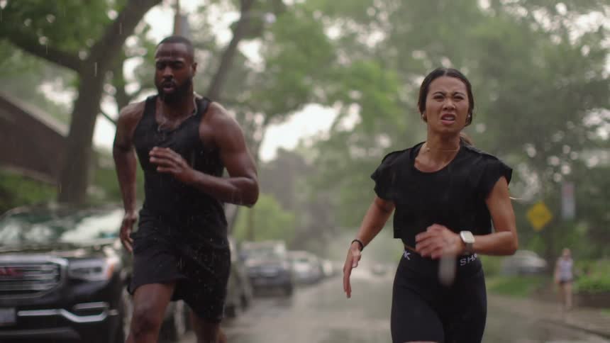 A man and woman run down a neighborhood street in the rain
