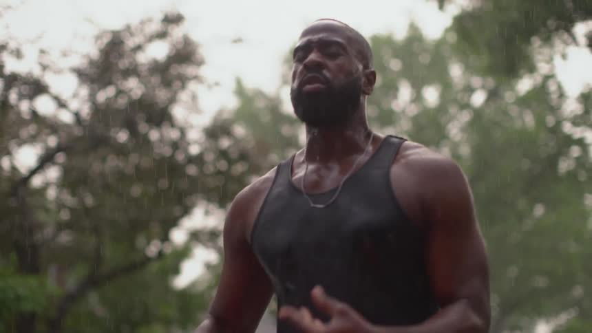 A man runs through the rain outdoors during the day before stopping to rest