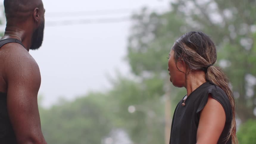 A man and woman in athletic wear congratulate one another as they catch their breath while standing outdoors on a neighborhood street in the rain