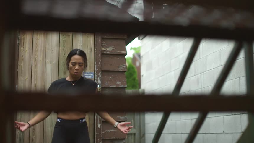 A woman jumps are shakes her arms out in front of a staircase outside